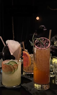 three different types of cocktails on a table in a dark room with other drinks