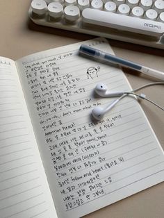 an open notebook with earbuds on it next to a keyboard