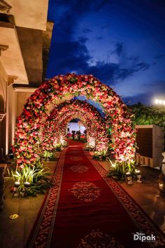 an archway decorated with red flowers and greenery at night, lit up by candles