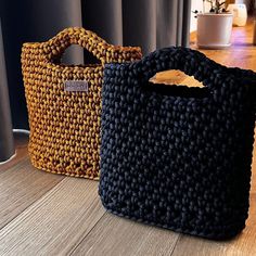 two knitted bags sitting on top of a wooden floor next to a window with curtains