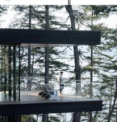 two people standing on the deck of a house in the woods with trees around them