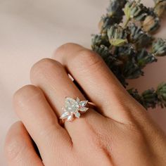 a woman's hand with a ring on it and some flowers in the background