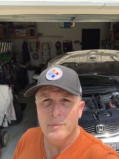 a man in an orange shirt and hat standing next to a car