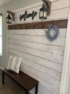 a bench sitting in front of a wooden wall with hooks on it and a welcome sign above the bench