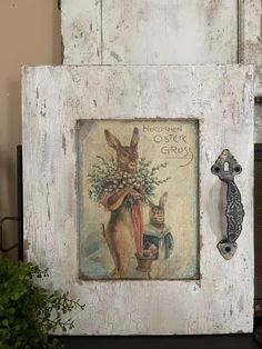 an old wooden frame with a rabbit and flowers on it, next to a potted plant