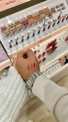 a person with their hand on the wrist of another person in front of some nail polish samples