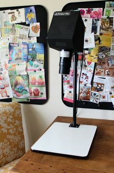 a laptop computer sitting on top of a wooden table next to a wall covered in pictures