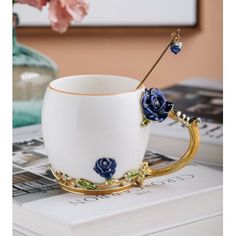 a white coffee cup with blue flowers on the rim and gold trimmings sitting on top of a book