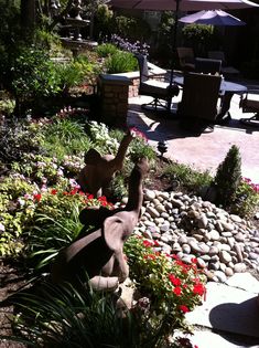 an elephant statue sitting in the middle of a garden with flowers and plants around it