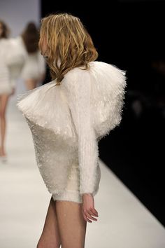 a model walks down the catwalk in a short white dress with feathers on it