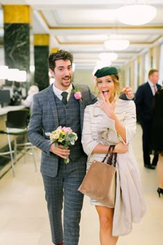 a man and woman are walking down the hall with flowers in their hand while smiling