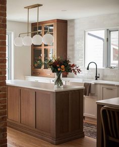 an instagramted photo of a kitchen with wooden cabinets and white counter tops, along with flowers in a vase on the island