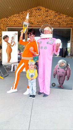 two people in costumes standing next to a small child wearing an orange astronaut suit and holding a bottle