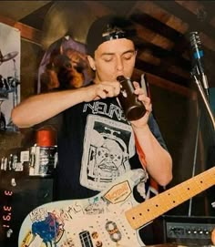 a young man is drinking from a bottle while playing an electric guitar and singing into a microphone