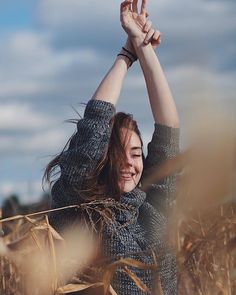 a woman standing in a wheat field holding her hands up to the sky and smiling