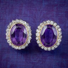 A glamorous pair of antique Victorian cluster earrings built around two regal purple amethysts (approx. 5ct each) bezel set in the centre of a halo of twinkling old mine cut diamonds (approx. 2ct total). Amethyst is considered a stone of protection, clarity and tranquillity and has been highly esteemed throughout the ages for its stunning beauty and deep violet colouring which has adorned regal jewellery all around the world, from ancient Egypt to the British crown jewels. The pair is a union of Vintage Amethyst Purple Earrings, Luxury Purple Round Earrings, Purple Fine Jewelry Earrings For Formal Occasions, Luxury Purple Earrings For Anniversary, Purple Oval Earrings For Weddings, Formal Purple Round Earrings, Elegant Purple Clip-on Earrings, Formal Purple Diamond Earrings, Formal Purple Clip-on Jewelry