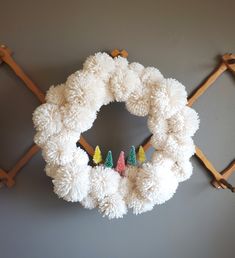 a white wreath hanging on the wall with small christmas trees in front of it,