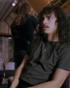 a man with long curly hair sitting in a chair next to a woman and looking off into the distance