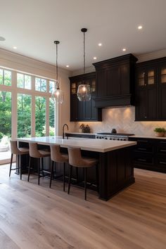 a large kitchen with black cabinets and an island in front of a window that has lights hanging from the ceiling