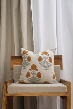 a pillow sitting on top of a wooden chair next to a window with curtains behind it