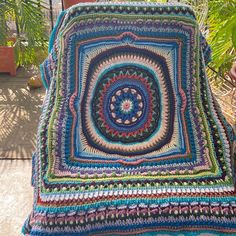 a crocheted blanket sitting on top of a wooden bench next to a potted plant