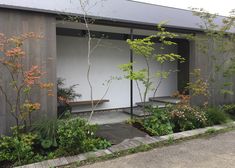 an outdoor area with trees, plants and benches on the side of the building in front of it