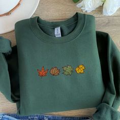 Introducing our Maple Leaves Embroidered Sweatshirt 2D Crewneck Sweatshirt – the perfect gift for your beloved family. This exceptional piece of clothing seamlessly blends style, comfort, and warmth, making it a must-have addition to your wardrobe. Let us take you on a journey through the exquisite details, remarkable features, and numerous benefits that this sweatshirt offers. The Maple Leaves Embroidered Sweatshirt is crafted with meticulous attention to detail. The beautiful maple leaf Casual Fleece T-shirt For Fall, Fall Green Tops With Embroidered Graphics, Green Tops With Embroidered Graphics For Fall, Green Embroidered Tops For Fall, Casual Fall Sweater With Custom Embroidery, Embroidered Green Sweatshirt For Fall, Casual Embroidered Fall T-shirt, Casual Tops With Custom Embroidery For Fall, Casual Embroidered T-shirt For Fall