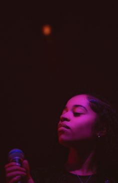 a woman holding a microphone in her right hand and looking up at the sky with bright lights behind her