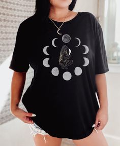 "Women's Goddess Moon Phases T-Shirt For an oversized tee, it is recommended to go up 1 size. For a T-Shirt Dress, it is recommended to go up 2 sizes.  However, it is still important to double-check the measurements in the sizing chart provided in the listing photos to ensure a perfect fit. ♥ DETAILS ♥ .: Classic fit .: Runs true to size .: Tear-away label .: Dual side seams hold the garment's shape for longer.  .: 7/8\" rib collar - Ribbed knit makes the collar highly elastic and helps retain its shape .: Shoulders have taping for a better fit over time ♥ SIZING ♥ - Please refer to the sizing chart in the listing photos to determine your size. - For a larger bust or a looser fit, it is recommended to size up. - For a t-shirt dress, it is recommended to size up 2 sizes. - For a more accura Graphic Tee With Moon Print For Streetwear, Short Sleeve Moon Print T-shirt For Streetwear, Black Moon Print Graphic Tee, Black Graphic Tee With Moon Print, Black Short Sleeve T-shirt With Moon Print, Relaxed Fit Short Sleeve T-shirt With Moon Print, Moon Print Relaxed Fit Crew Neck T-shirt, Goddess Moon, Streetwear Tshirt Design