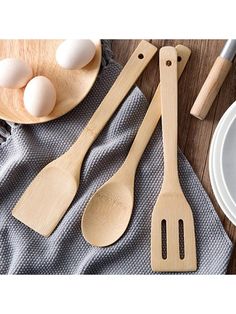 wooden spoons and spatulas on a table with eggs in the bowl next to them