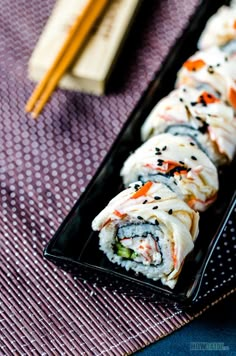 sushi rolls on a black plate with chopsticks