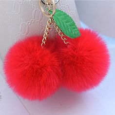 red pom - pom keychain with green leaf on it sitting on a white surface