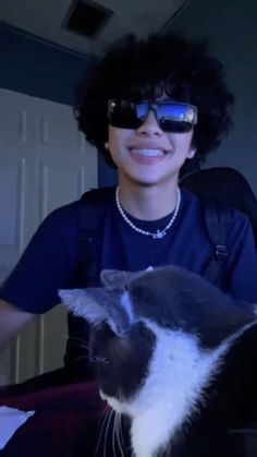 a person wearing sunglasses with a cat in front of them on their lap and smiling at the camera