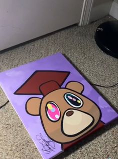 a painting of a teddy bear with a graduation cap on it's head is sitting on the floor