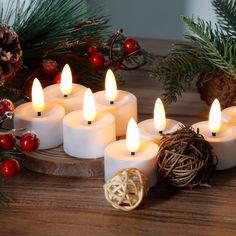 lit candles sitting on top of a wooden table next to pine cones and evergreen branches