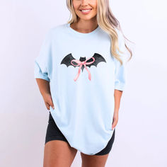 Get ready to swoon over our Black Bat Pink Bow T-Shirt, a perfect blend of spooky and cute for your Halloween festivities! Featuring an adorable black bat design with a charming pink bow, this t-shirt is sure to be a hit whether you're attending a Halloween party, heading to a pumpkin patch, or just getting into the spirit of the season. Made from 100% ring-spun cotton, this tee offers a soft-washed, garment-dyed fabric that delivers exceptional coziness. Character Print Short Sleeve Top For Costume Party, Short Sleeve Tops With Character Print For Costume Party, Character Print Top For Costume Party With Short Sleeves, Spooky Short Sleeve Tops For Costume Party, Witchy Crew Neck Top For Halloween, Witchy Crew Neck Halloween Tops, Spooky Character Print Tops For Costume Party, Casual Short Sleeve Tops For Costume Party, Spooky Cotton Tops For Costume Party