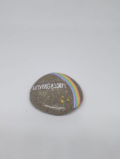 a rock with the words universe on it and rainbows painted on it, against a white background