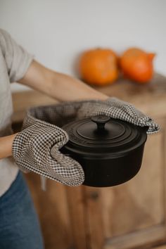 a woman holding a black pot in front of some oranges