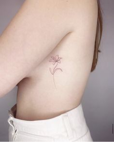 a woman's breast with a small flower tattoo on her left side ribcage