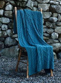 a blue blanket sitting on top of a wooden chair in front of a stone wall