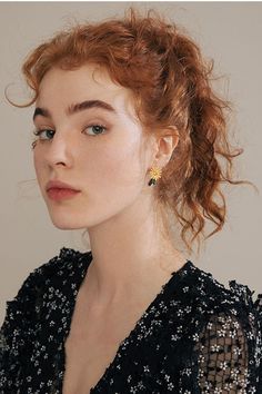 a woman with red hair wearing a black dress and gold earring on her left ear