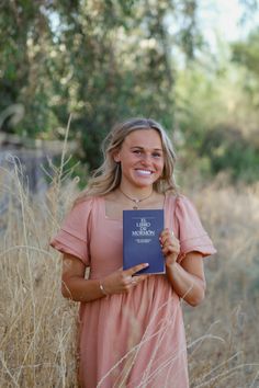 a woman standing in tall grass holding a book