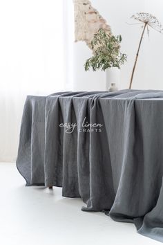 an image of a table setting with grey linens on it and a potted plant in the background