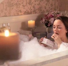 a woman sitting in a bathtub with candles on the side and her mouth open