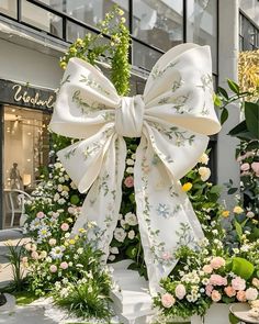 a large white bow sitting on top of a lush green plant covered ground in front of a building