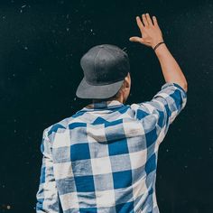 a man wearing a blue and white checkered shirt raises his hands in the air