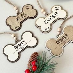 three personalized wooden dog tags hanging from a christmas tree with pine cones and berries