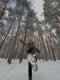 a snowboarder doing a trick in the air near some pine trees and snow