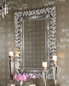 a mirror sitting on top of a table next to two candles and some pink flowers