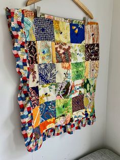 a multicolored patchwork quilt hanging on a wall next to a bed with a wooden hanger